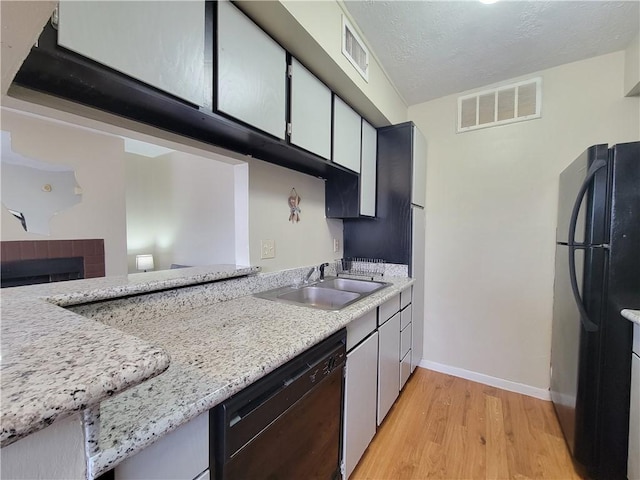 kitchen with sink, light hardwood / wood-style floors, black appliances, light stone countertops, and a textured ceiling