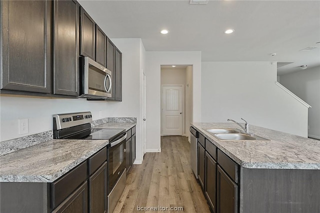 kitchen with sink, an island with sink, dark brown cabinets, light hardwood / wood-style floors, and stainless steel appliances