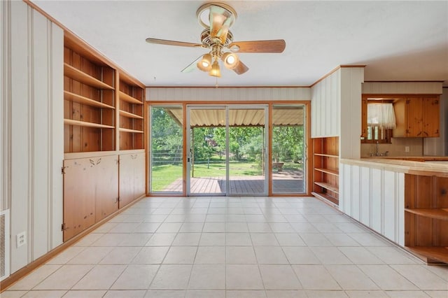 unfurnished living room featuring crown molding, built in shelves, and ceiling fan