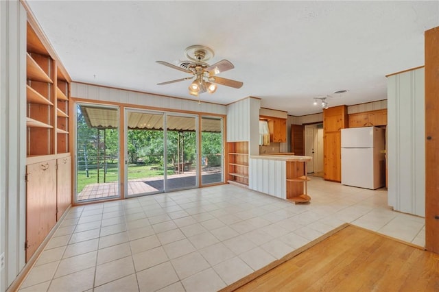 kitchen with freestanding refrigerator, a ceiling fan, a peninsula, light tile patterned floors, and wood walls