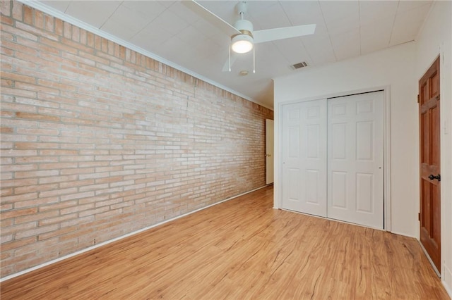 unfurnished bedroom with brick wall, wood finished floors, a closet, and a ceiling fan