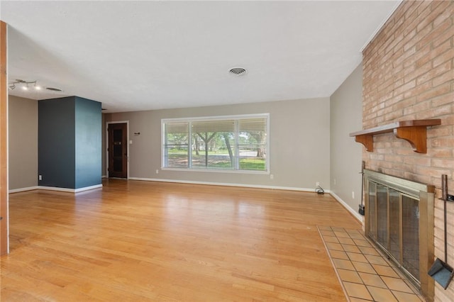 unfurnished living room featuring a brick fireplace, light wood-style flooring, and baseboards