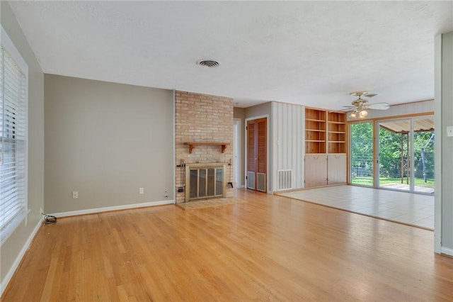 unfurnished living room featuring light wood-style flooring, ceiling fan, baseboards, built in shelves, and a textured ceiling
