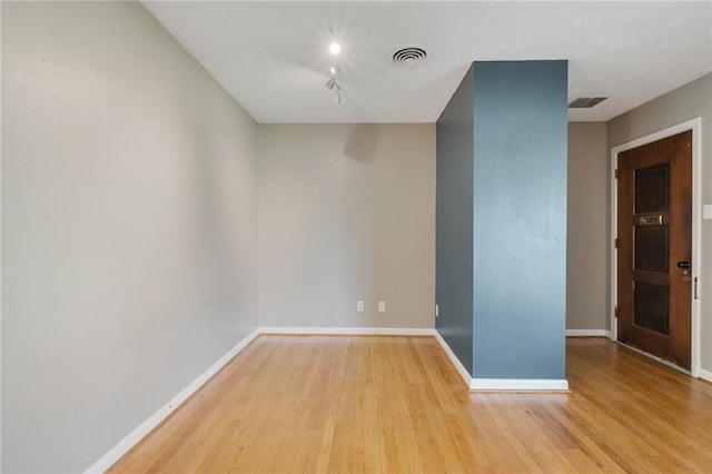 empty room with wood finished floors, baseboards, and track lighting