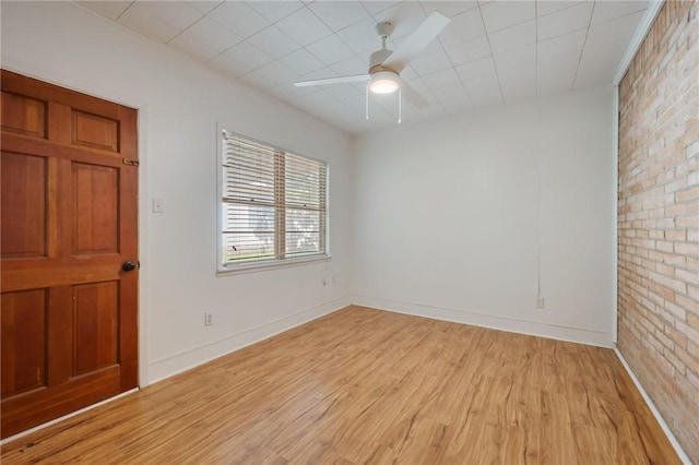 empty room with light wood-type flooring, ceiling fan, brick wall, and baseboards