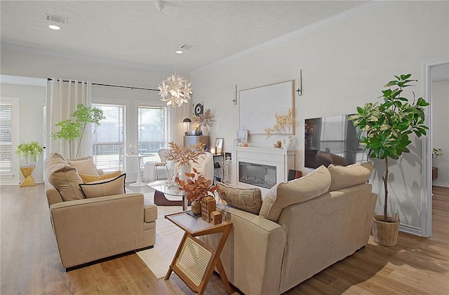 living room with light wood-type flooring, ornamental molding, and a chandelier