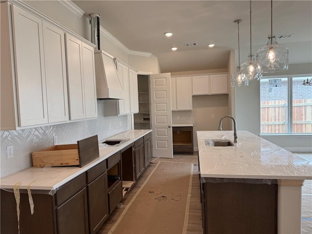 kitchen featuring a sink, visible vents, backsplash, and an island with sink