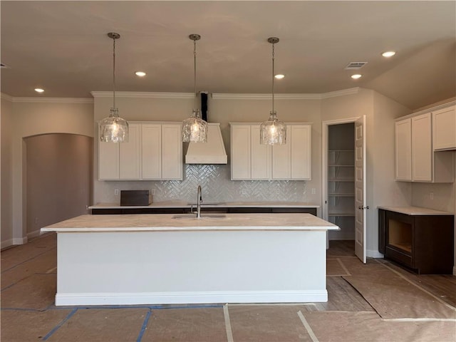 kitchen with tasteful backsplash, visible vents, a sink, white cabinets, and a kitchen island with sink