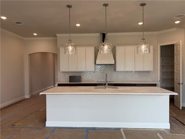 kitchen with tasteful backsplash, white cabinets, an island with sink, and visible vents