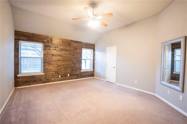 carpeted empty room featuring ceiling fan, wood walls, and vaulted ceiling