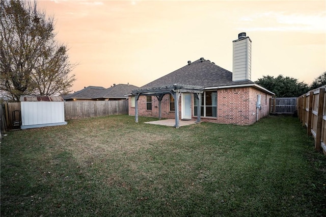 back house at dusk featuring a patio, a shed, and a lawn