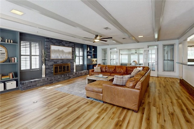 living room featuring a brick fireplace, ceiling fan, beam ceiling, built in features, and light hardwood / wood-style floors