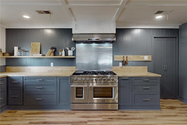 kitchen featuring wall chimney exhaust hood, light hardwood / wood-style floors, range with two ovens, and butcher block counters