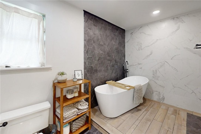 bathroom featuring a washtub, toilet, and tile walls