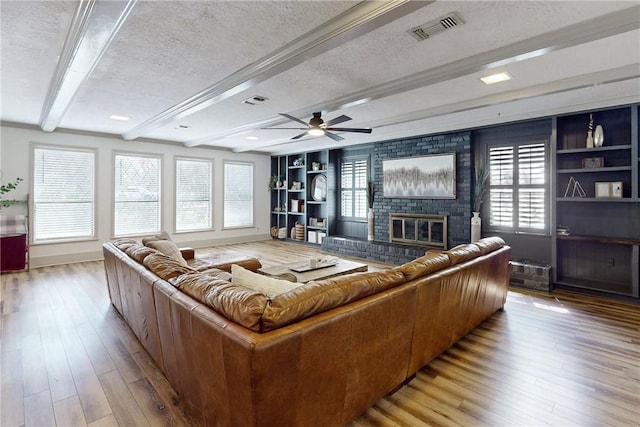 living room with a brick fireplace, light hardwood / wood-style flooring, built in features, a textured ceiling, and beam ceiling