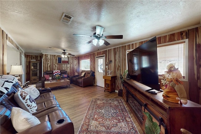 living room featuring ceiling fan, crown molding, a textured ceiling, wooden walls, and light wood-type flooring