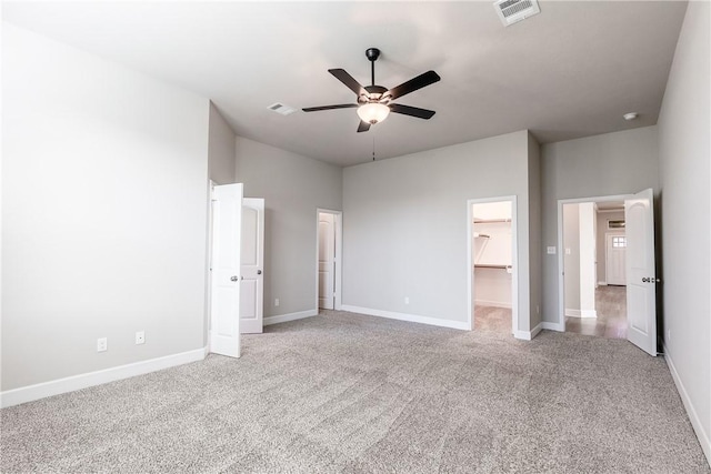 unfurnished bedroom featuring light carpet, a walk in closet, ceiling fan, a towering ceiling, and a closet