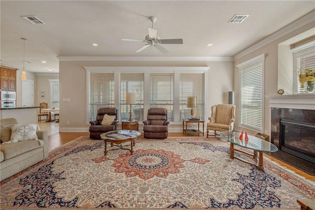 living room featuring a high end fireplace, light hardwood / wood-style flooring, ceiling fan, and crown molding