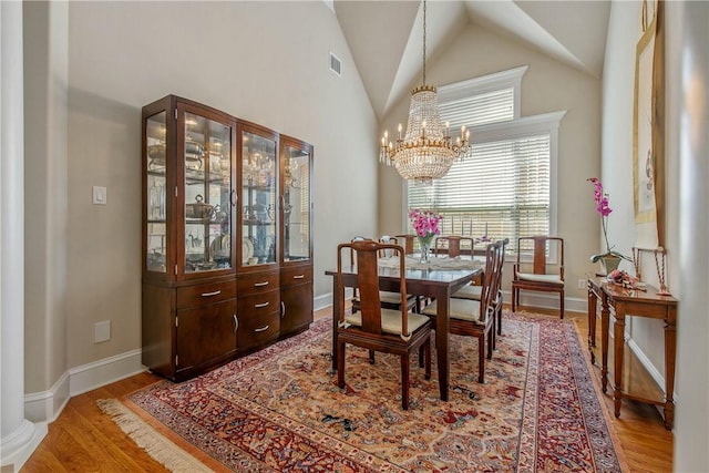 dining room with light wood-type flooring, high vaulted ceiling, and a chandelier