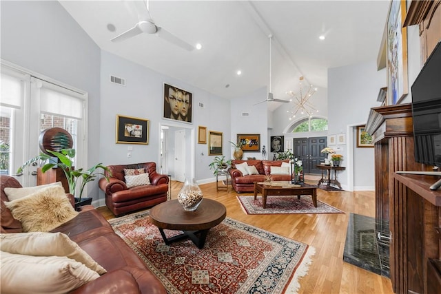 living area featuring a ceiling fan, high vaulted ceiling, light wood-type flooring, visible vents, and baseboards