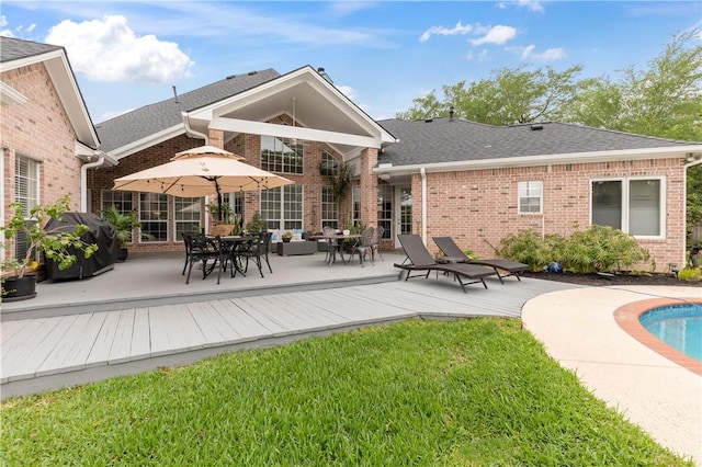 rear view of property featuring brick siding, roof with shingles, a deck, and a lawn