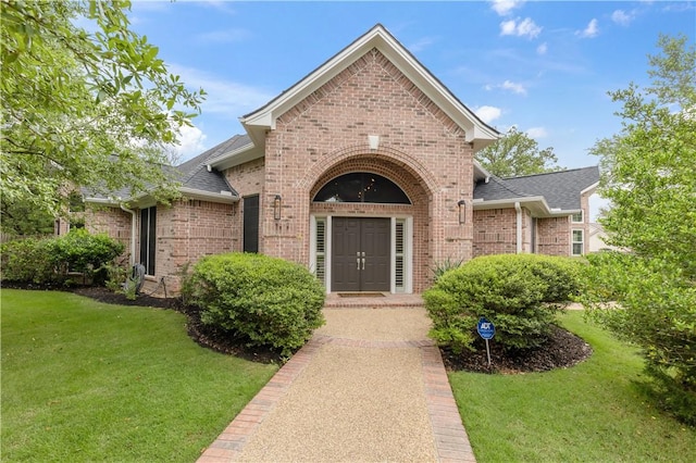 doorway to property with brick siding, roof with shingles, and a lawn