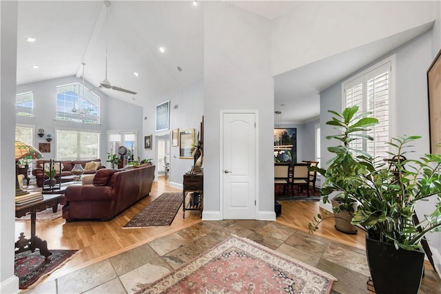 living room featuring stone tile flooring, a ceiling fan, a healthy amount of sunlight, and high vaulted ceiling