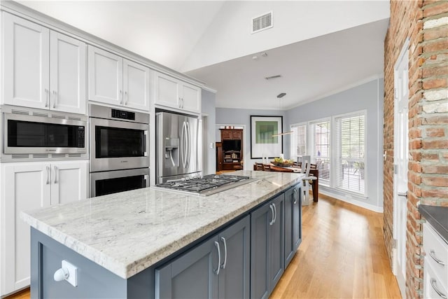 kitchen featuring light wood finished floors, visible vents, light stone countertops, appliances with stainless steel finishes, and vaulted ceiling