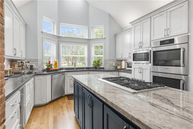 kitchen with a sink, stainless steel appliances, decorative backsplash, and high vaulted ceiling