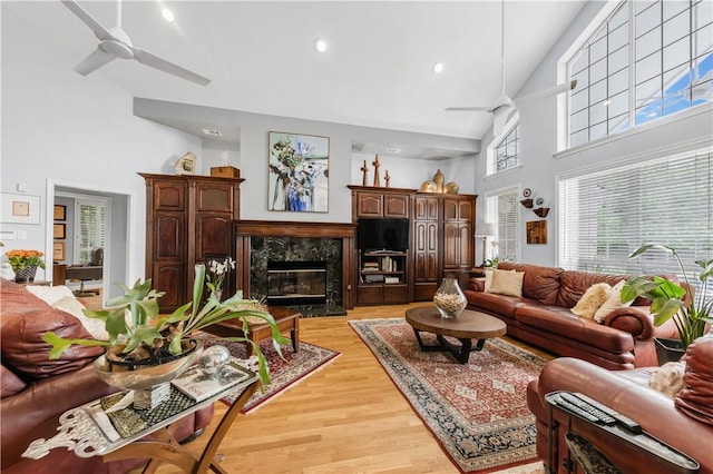 living area featuring light wood-style floors, a high end fireplace, ceiling fan, and high vaulted ceiling