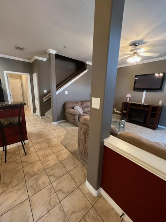 living room featuring light tile patterned flooring, ceiling fan, ornamental molding, and a fireplace