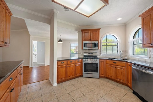 kitchen with stainless steel appliances, brown cabinetry, a sink, and backsplash