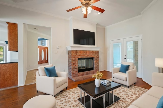 living area featuring french doors, crown molding, a ceiling fan, a brick fireplace, and wood finished floors