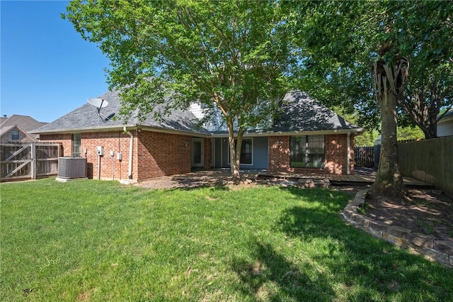 rear view of property with a lawn, a fenced backyard, central AC unit, and brick siding
