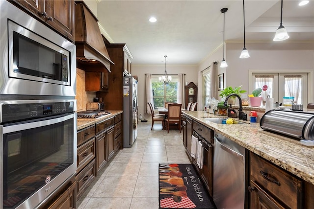 kitchen with premium range hood, light stone counters, decorative light fixtures, and appliances with stainless steel finishes