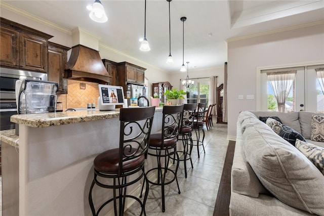 kitchen featuring backsplash, light stone counters, a kitchen bar, and premium range hood