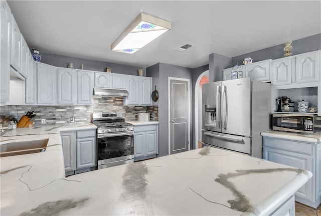 kitchen with appliances with stainless steel finishes, sink, white cabinets, decorative backsplash, and light stone counters