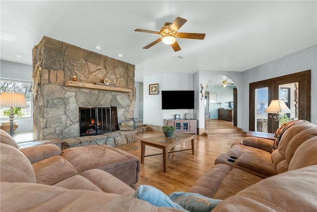 living room featuring a stone fireplace, light hardwood / wood-style floors, and ceiling fan