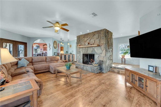 living room featuring a stone fireplace, light hardwood / wood-style floors, and ceiling fan