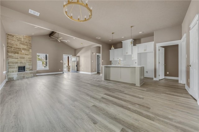 unfurnished living room featuring a stone fireplace, high vaulted ceiling, light wood-type flooring, beamed ceiling, and ceiling fan with notable chandelier