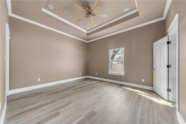 empty room with ceiling fan, ornamental molding, a raised ceiling, and light hardwood / wood-style flooring