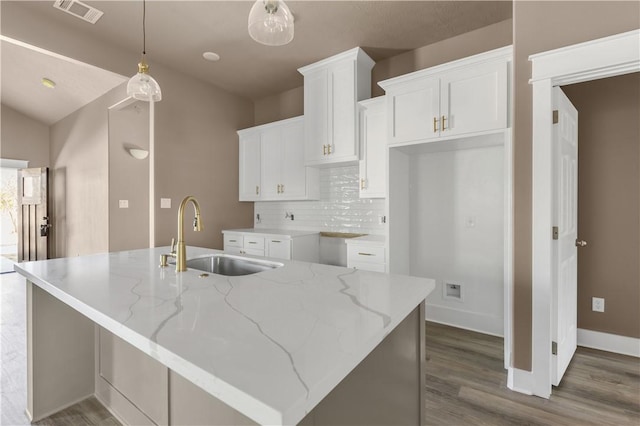 kitchen featuring a kitchen island with sink, sink, light stone counters, and white cabinets