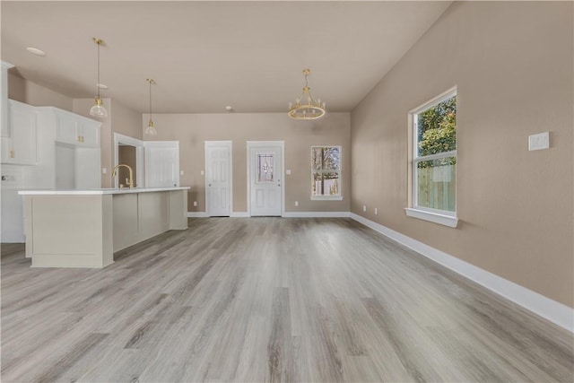 kitchen with pendant lighting, sink, white cabinetry, and an island with sink