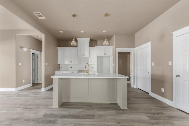 kitchen with tasteful backsplash, white cabinetry, sink, and a center island with sink