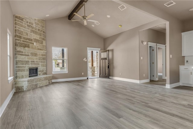 unfurnished living room with high vaulted ceiling, a fireplace, light wood-type flooring, ceiling fan, and beam ceiling