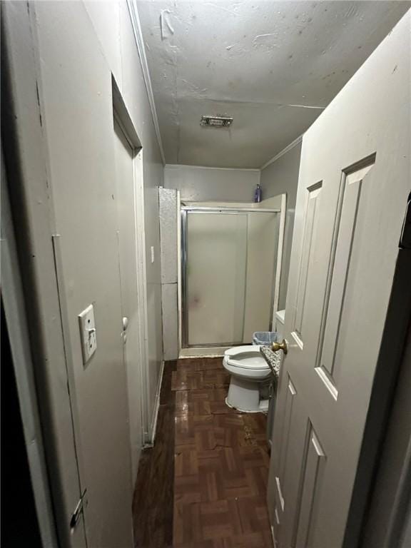 bathroom featuring parquet floors, a shower with shower door, and toilet