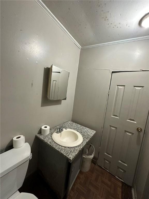 bathroom with vanity, toilet, ornamental molding, and parquet flooring