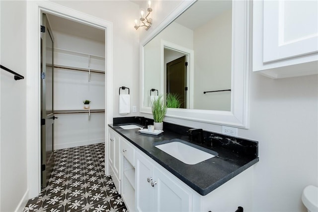 full bathroom with tile patterned floors, a walk in closet, a sink, double vanity, and baseboards