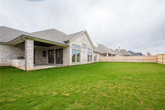 back of property featuring brick siding, roof with shingles, a lawn, a fenced backyard, and a patio area