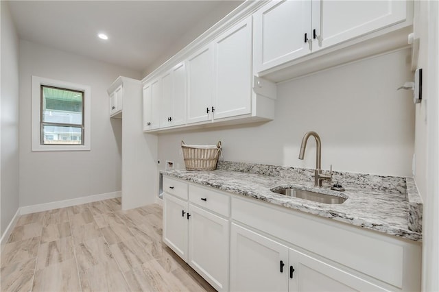 kitchen with a sink, white cabinetry, recessed lighting, baseboards, and light stone countertops